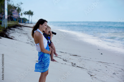 Mom, holding little toddler boy with binoculars, observing dolphins