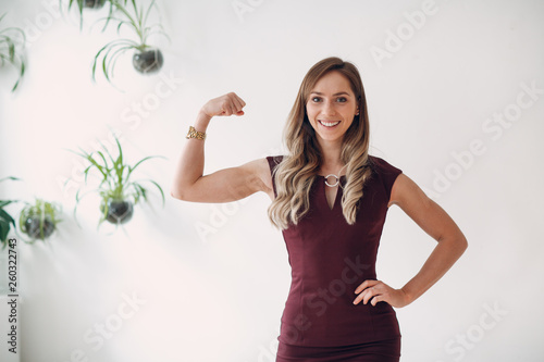 Portrait close up of young sporty woman in dress at bright room. Byceps fit in office. photo