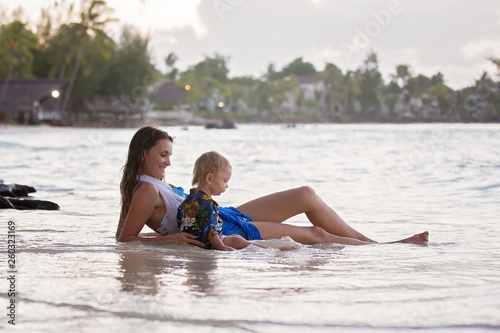 Happy beautiful fashion family, children, dressed in hawaiian shirts, playing together on the beach on sunset