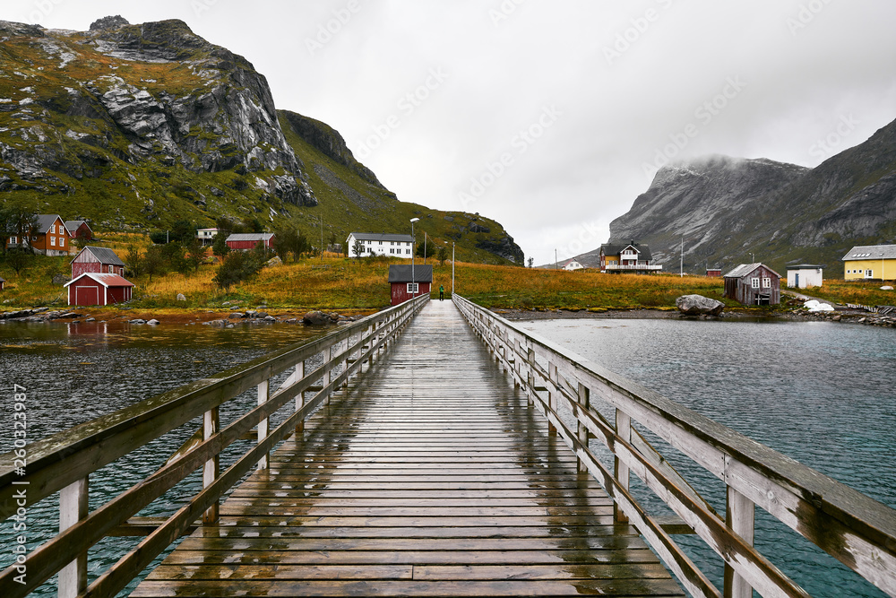 Obraz premium Wooden bridge on the water leading to the village Vinstad and Bunes Beach in moskenesoya on Lofoten Islands in Norway. The village consists of several traditional cabins in the mountains.