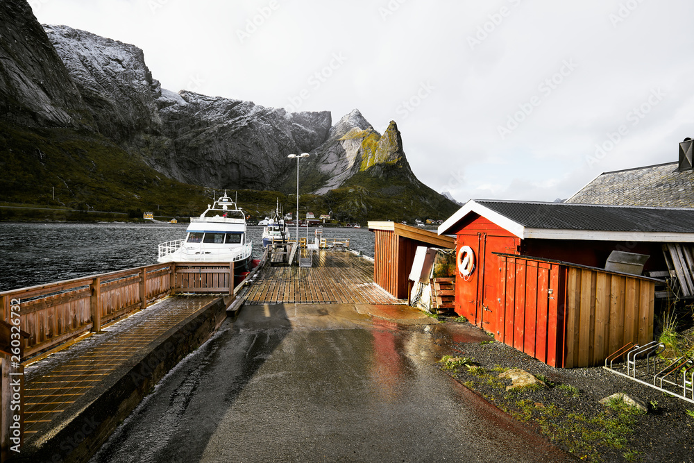 Scenic view of the harbor in Reine with a boat and the jetty at the coast on Lofoten Islands in Norway. The harbor is also the ferry station for tourists to be driven to Vinstad and Bunes Beach.