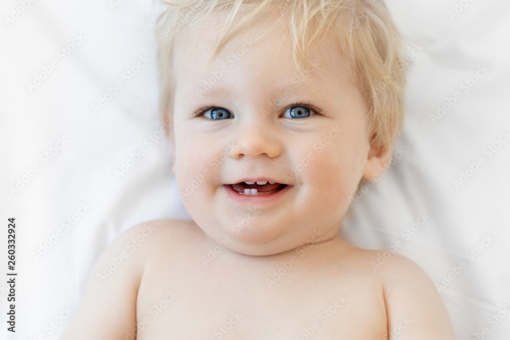 Close up of smiling blonde baby laying on white bed Close up of smiling blonde baby laying on white bed