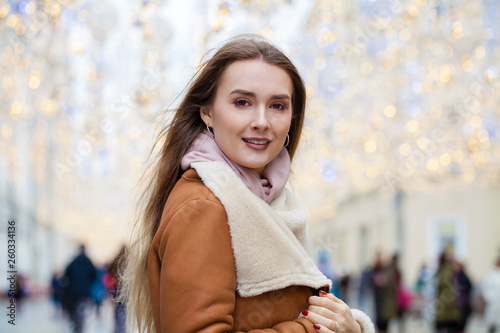 Happy Beautiful woman in a sheepskin coat in the center of the Christmas winter street
