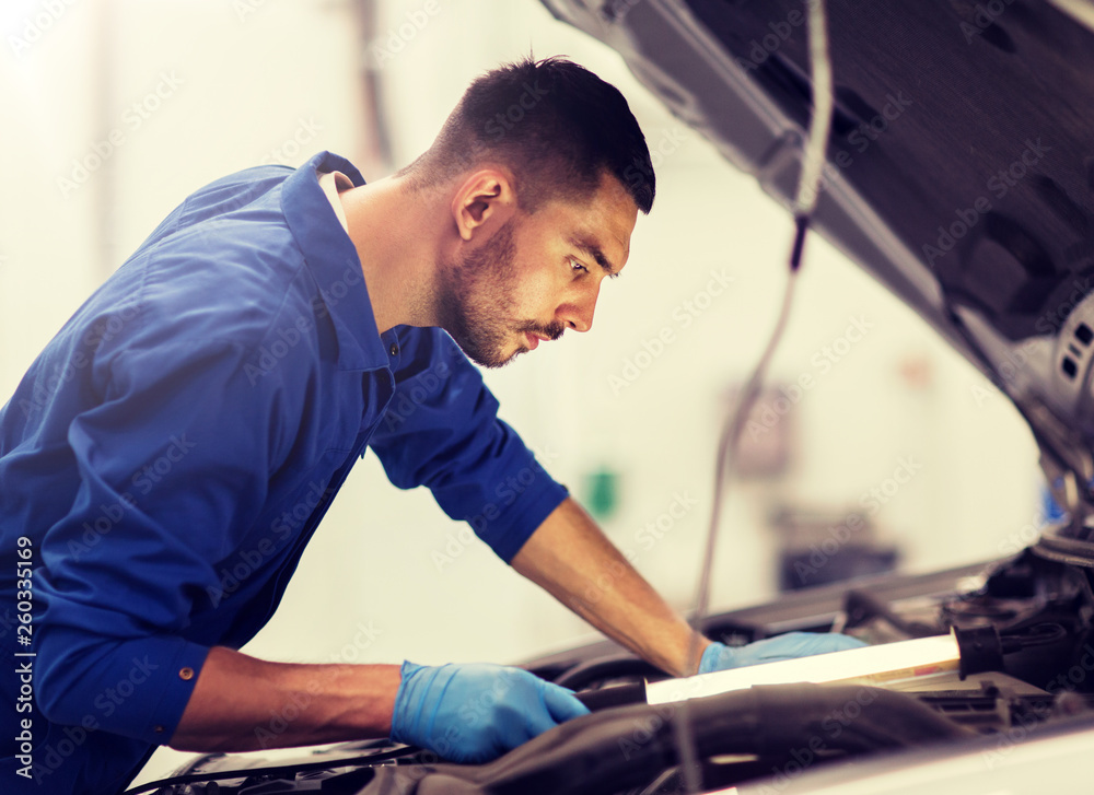 car service, repair, maintenance and people concept - auto mechanic man with lamp working at workshop car service, repair, maintenance and people concept - auto mechanic man with lamp working at workshop