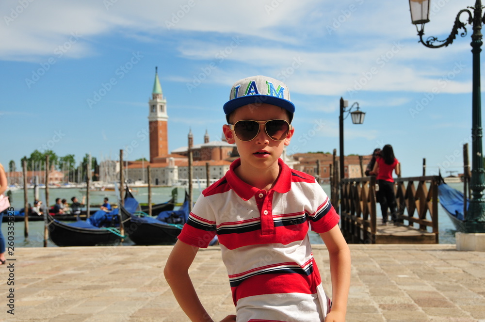Obraz premium Boy in polo shirt with cap and sunglasses in front of the landmark of Venice