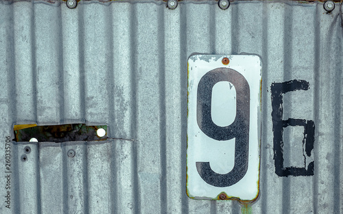 White Shabby Metal Plate With Black Nuber Nine and Six Nailed On Corrugated Old Iron Sheet photo