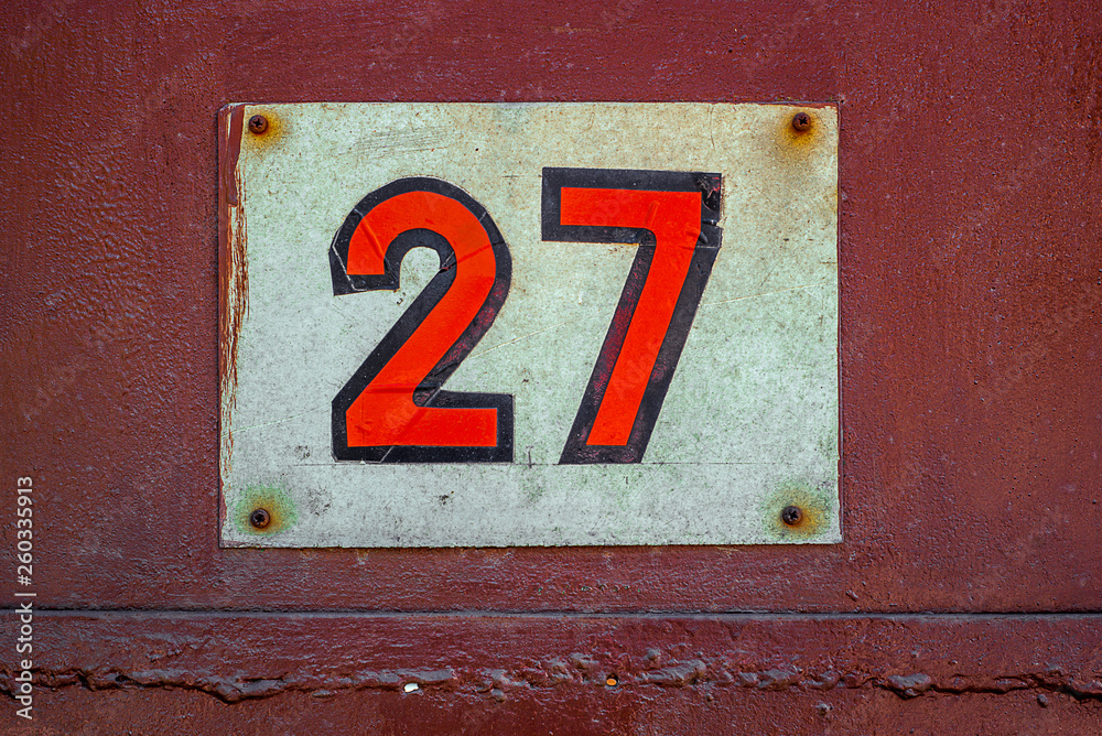 White Shabby Metal Plate With Red Nuber Twenty Seven Nailed On Red Metal Door White Shabby Metal Plate With Red Nuber Twenty Seven Nailed On Red Metal Door