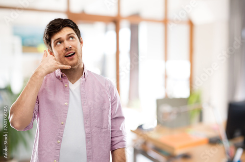 people concept - young man showing phone call gesture over office room background