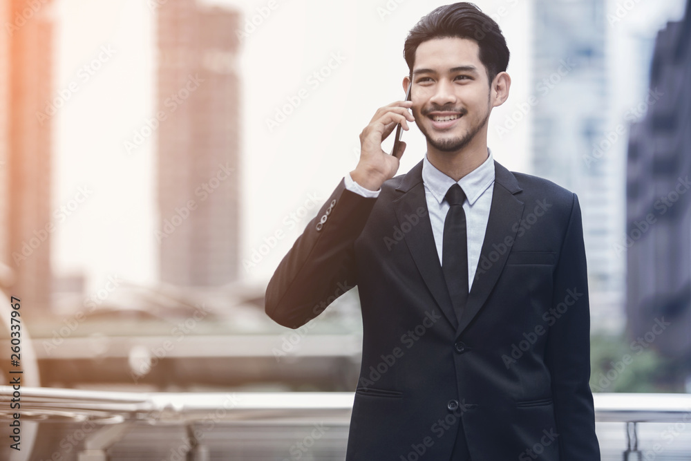 Young executive businessman using a mobile phone in the business district with skyscrapers buildings background Young executive businessman using a mobile phone in the business district with skyscrapers buildings background