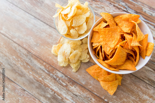 fast food, junk-food, cuisine and eating concept - close up of crunchy potato and corn crisps or nachos in bowls on wooden table