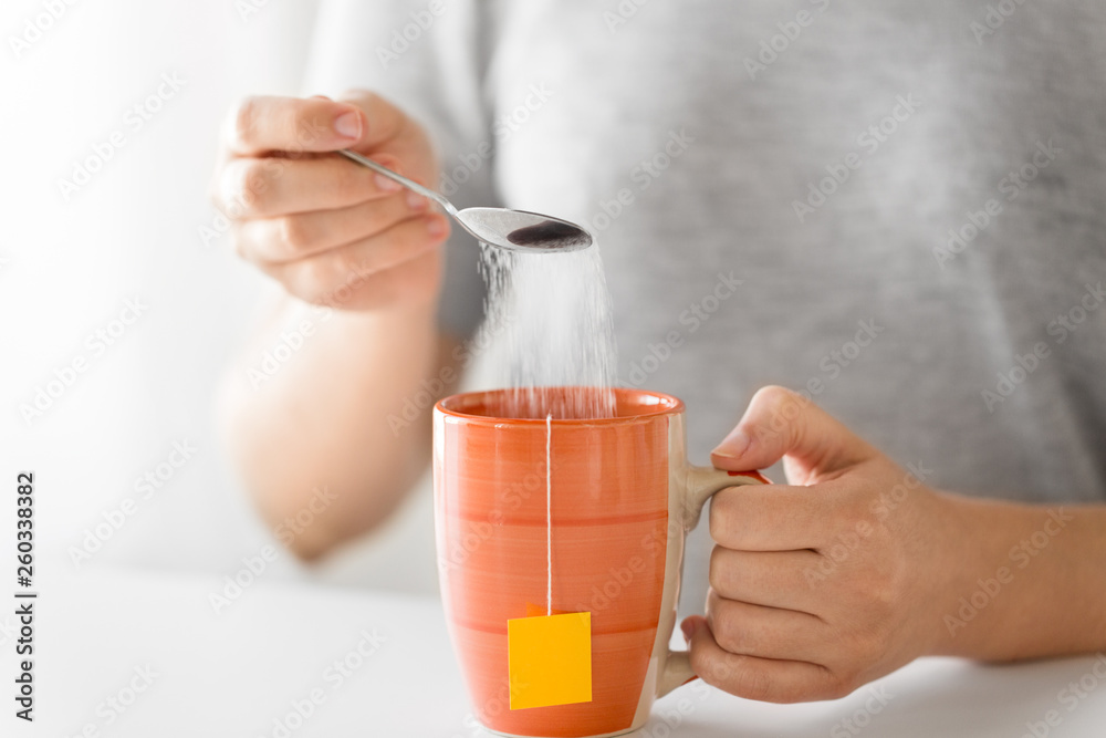 hot drinks concept - close up of woman adding sugar to cup of tea hot drinks concept - close up of woman adding sugar to cup of tea