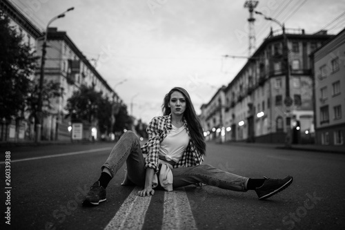 Girl in a plaid shirt and jeans. Girl posing sitting on the middle of the road. © mushegovdima