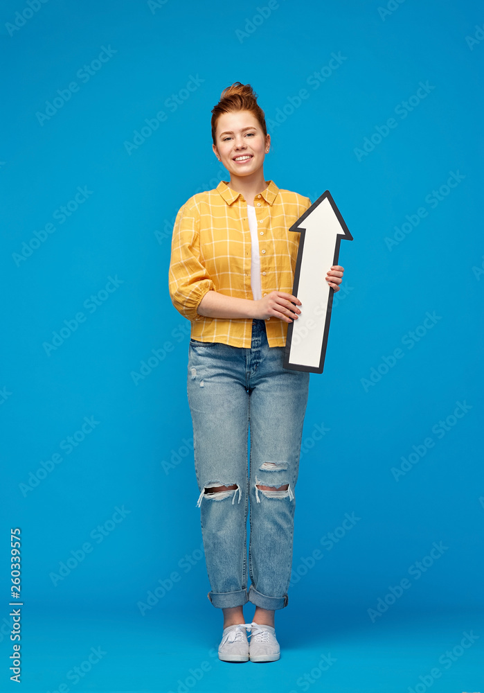direction and people concept - smiling red haired teenage girl in checkered shirt holding big white upwards thick arrow over bright blue background direction and people concept - smiling red haired teenage girl in checkered shirt holding big white upwards thick arrow over bright blue background