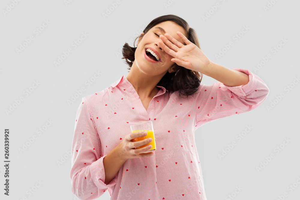 people and morning concept - happy yawning sleepy young woman in pajama with glass of orange juice over grey background people and morning concept - happy yawning sleepy young woman in pajama with glass of orange juice over grey background