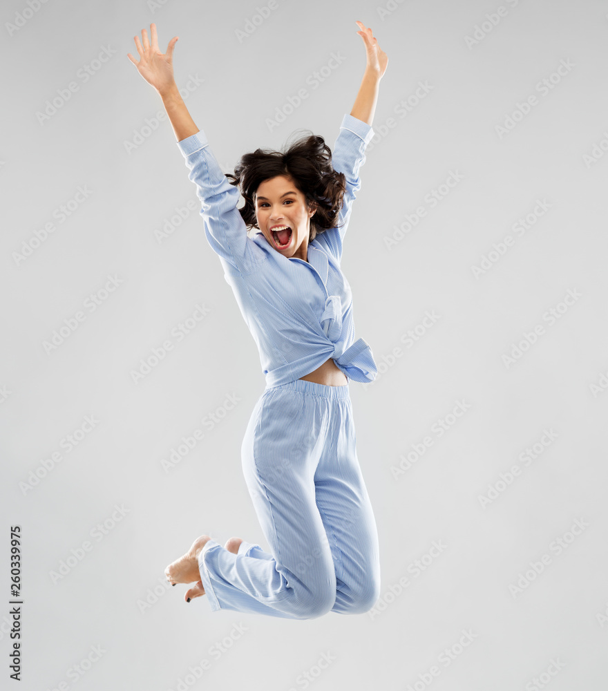 fun, people and bedtime concept - happy young woman full of energy in blue pajama jumping over grey background - obrazy, fototapety, plakaty 