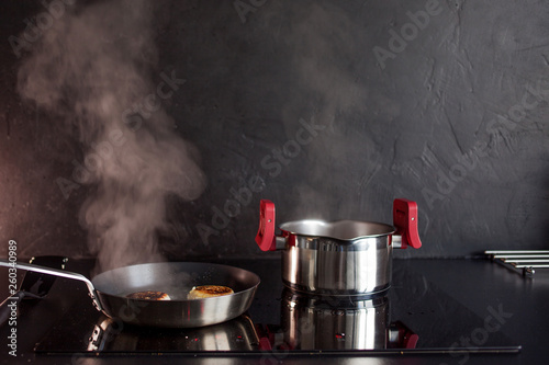 Frying pan and cooking pot on induction hob, steam rises. Black textured kitchen