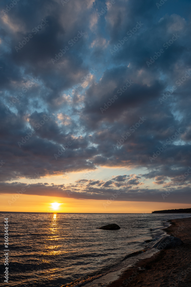 Obraz premium colorful sunset over calm sea beach with dark blue water and dramatic contrasty clouds