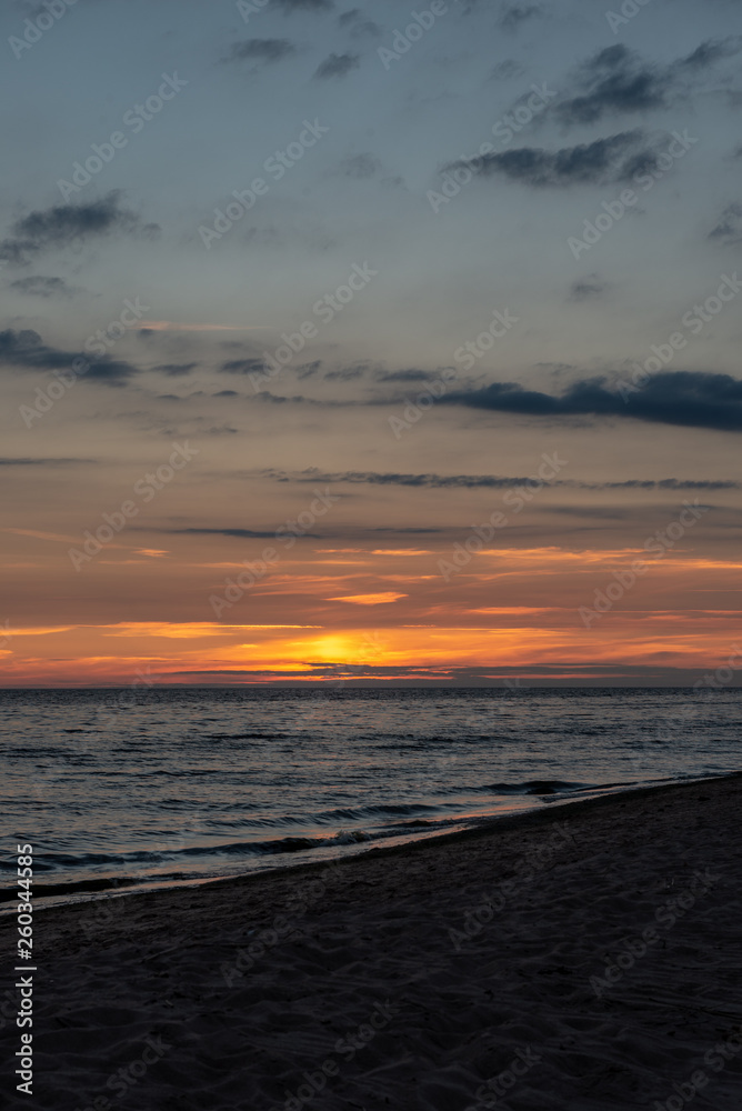 colorful sunset over calm sea beach with dark blue water and dramatic contrasty clouds