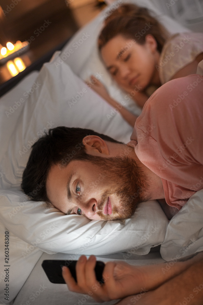 technology, internet addiction and cheat concept - man using smartphone at night while his girlfriend is sleeping technology, internet addiction and cheat concept - man using smartphone at night while his girlfriend is sleeping