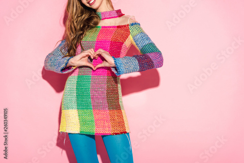 cropped view of cheerful girl showing heart-shape sign on pink
