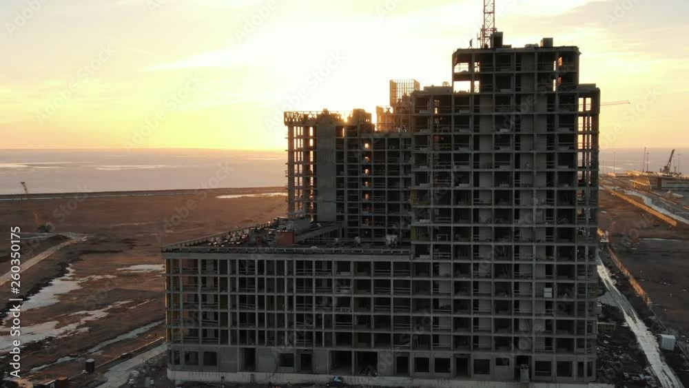 Flying of the construction of a multi-storey building on the background of sunset rays on the seashore Flying of the construction of a multi-storey building on the background of sunset rays on the seashore