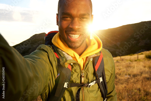happy black man hiking and taking selfie with sunset in background