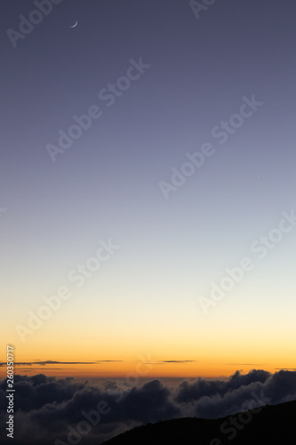 Crescent moon over the bright orange horizon lit by the last light of sunset at the Mauna Kea on Big Island, Hawaii, USA.