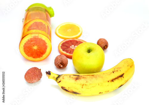 Sports bottle with lemonade from tropical fruits on a white background. Detox fruit infused water, citrus fruits .. Banana, apple, red orange, lychee. Top view, flat lay, copy space