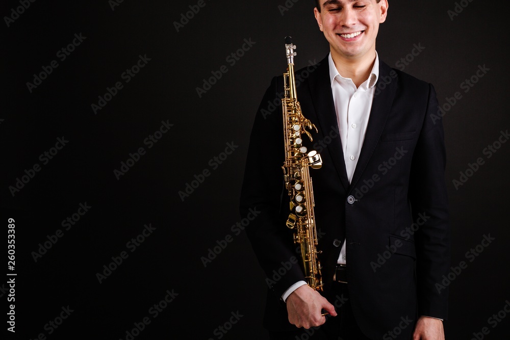 Naklejka premium Man saxophonist in black classic suit holding a soprano saxophone standing on a black background