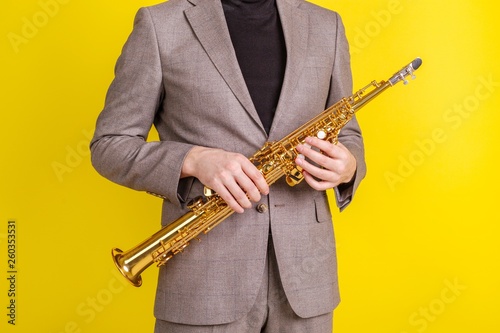 Saxophonist in classic clothes holding a soprano saxophone on a yellow background close-up