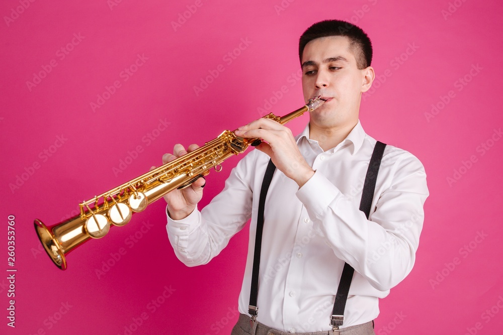 Fototapeta premium Saxophonist playing soprano saxophone standing on pink background
