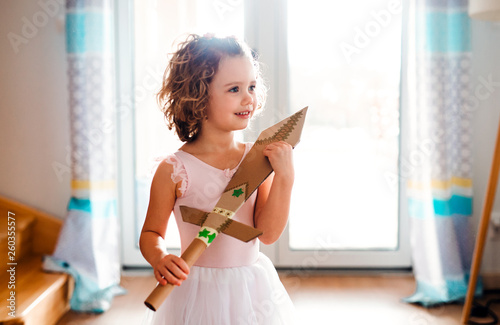 A small girl with a princess dress at home, holding a toy sword.