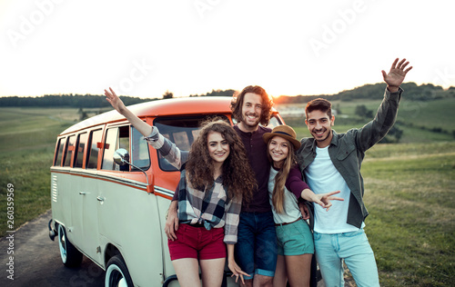 A group of young friends on a roadtrip through countryside, standing by a minivan. photo