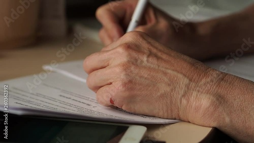 Aged woman of European appearance sitting at table is what a business contract. The signing of important legal document. Reading and familiarization with text on paper. Crucial moment. Close up