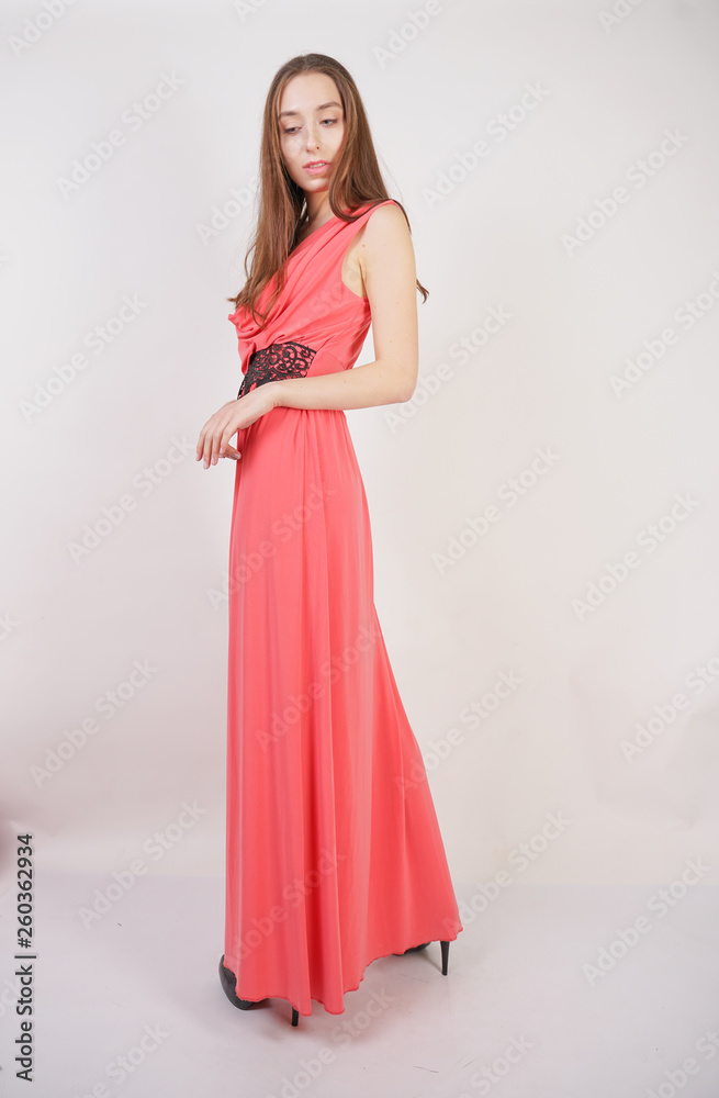 charming young girl in red evening long dress with black lace stands on a white background in the Studio