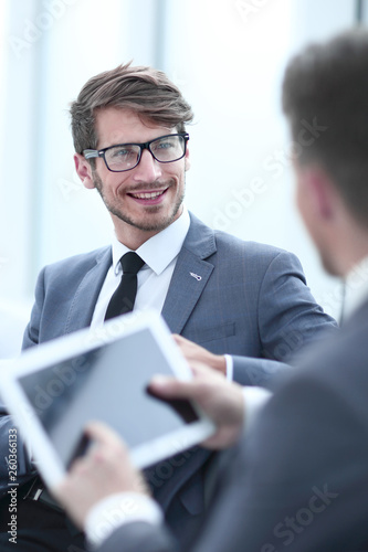 Image of two young businessmen using touchpad at meeting