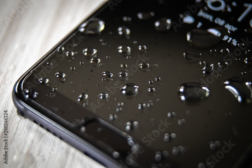 Front side of waterproof smartphone covered with drops of water