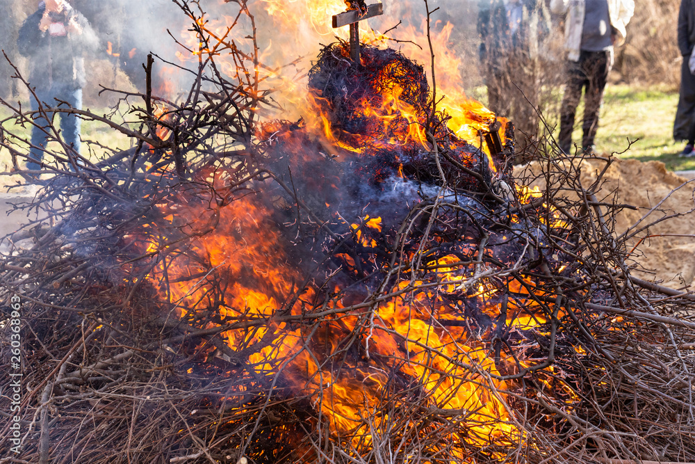 Flaming fire. Big bonfire in Shrovetide. Burning tree branches. People look at the fire. Pagan rite dedicated to the arrival of spring.