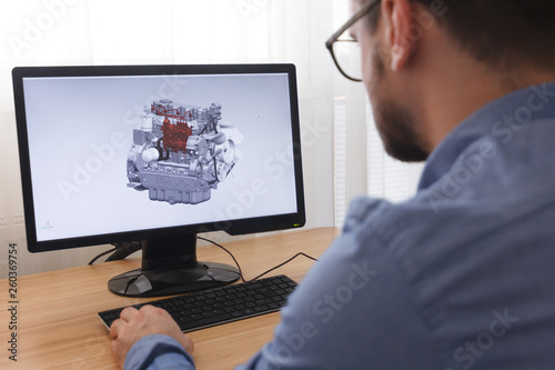 Engineer, Constructor, Designer in Glasses Working on a Personal Computer. He is Creating, Designing a New 3D Model of Car Engine, Motor in CAD Program. Freelance Work