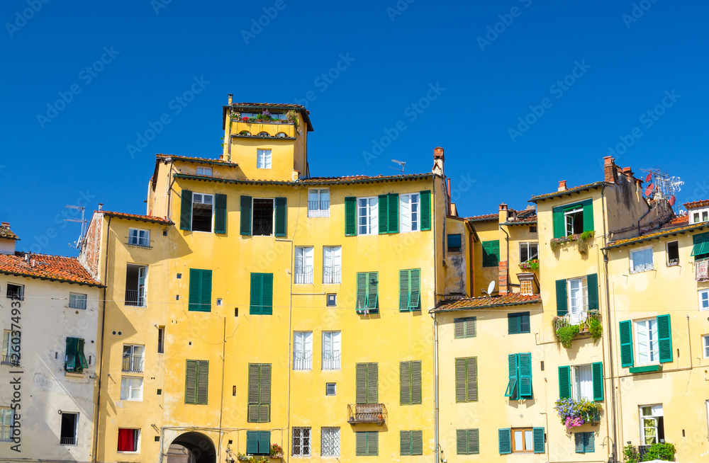 Wall of colorful buildings with shutter windows on Piazza dell Anfiteatro square in circus yard of medieval town Lucca historical centre, blue clear sky background, Tuscany, Italy