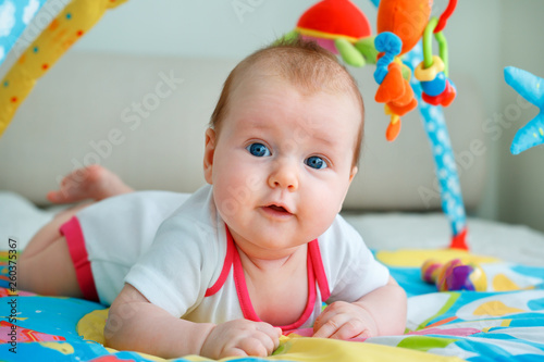 Adorable baby girl having fun with toys on colorful play mat