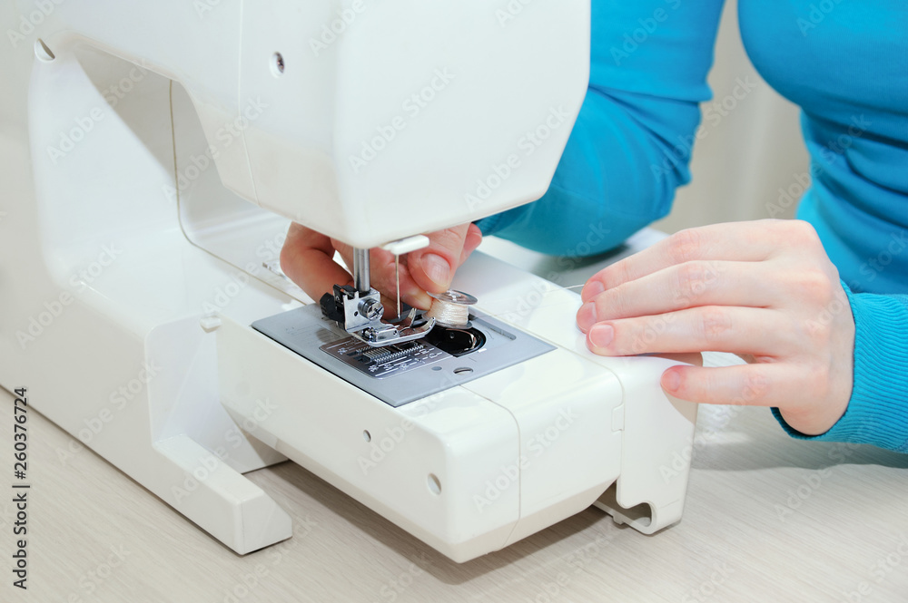 Caucasian girl inserts a bobbin with thread in the sewing machine. Close-up.