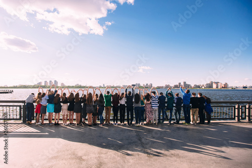 Group of young beautiful cheerful friends hugging by waist look into the panorama of the city. Concept of multinational friendship between teenagers boys and girls dressed fasionable clothes back view