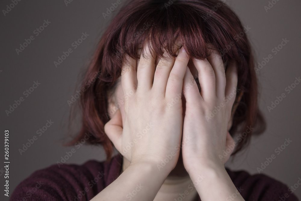 Red-haired woman having a headache or being embarrassed. Hands over the face. Human facial expression, emotion, feeling, sign symbol body language Red-haired woman having a headache or being embarrassed. Hands over the face. Human facial expression, emotion, feeling, sign symbol body language