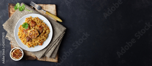 Oriental cuisine. Uzbek pilaf or plov from meat in a plate on wooden rustic board. Long format. Top view vith copy space.
