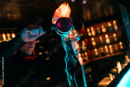 The bartender man, behind the bar, is preparing a burning cocktail