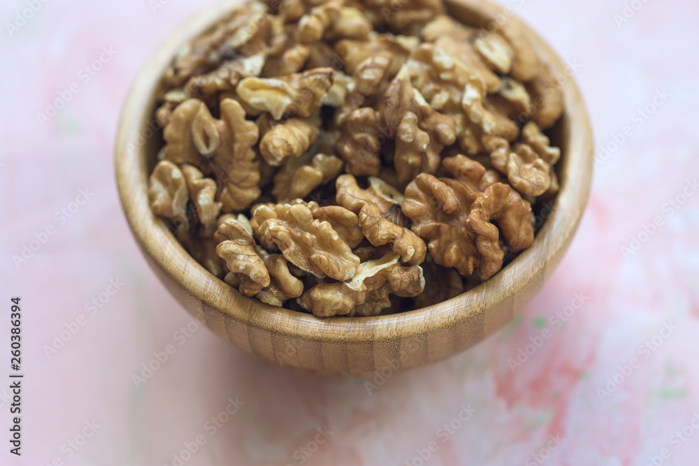 Walnuts kernels, peeled nuts in a wooden bowl on a pink background Walnuts kernels, peeled nuts in a wooden bowl on a pink background