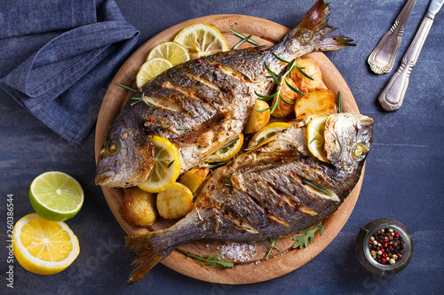Canvas Print Grilled fish with roasted potatoes, lemon and rosemary on wooden tray
