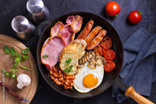 Full English or Irish breakfast with sausages, bacon, eggs, tomatoes, mushrooms and beans on black background