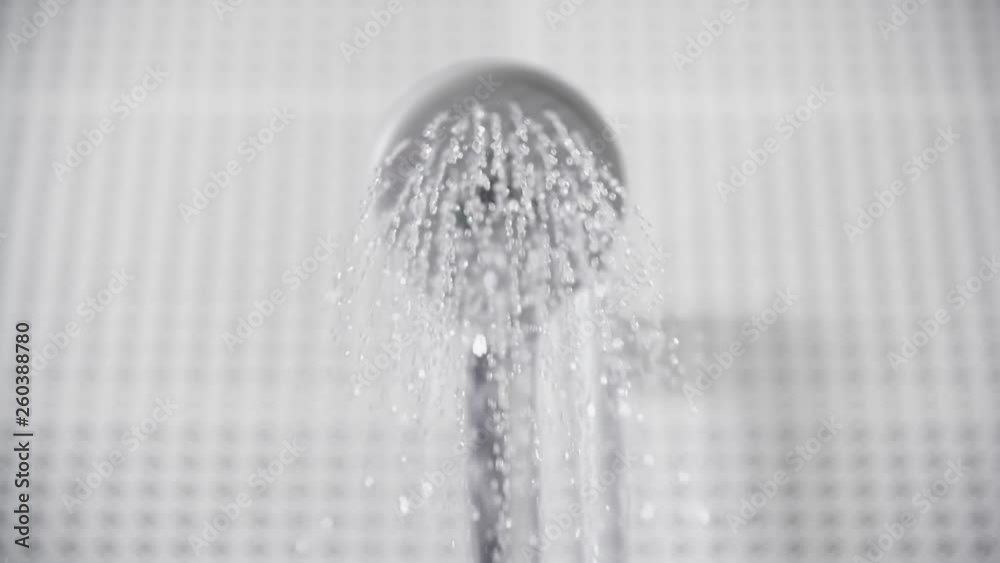 Close-up of turning on and off shower head in bathroom, white tiles with black pattern on the walls, focus on water sprays out and flowing slowly, falling drops